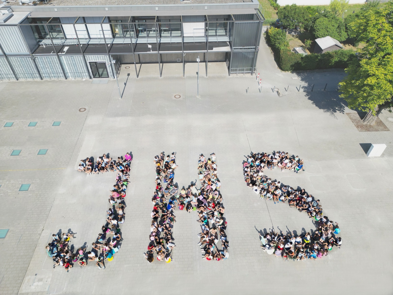 Kinder stehen auf den großen Buchstaben JHS auf dem Schulgelände